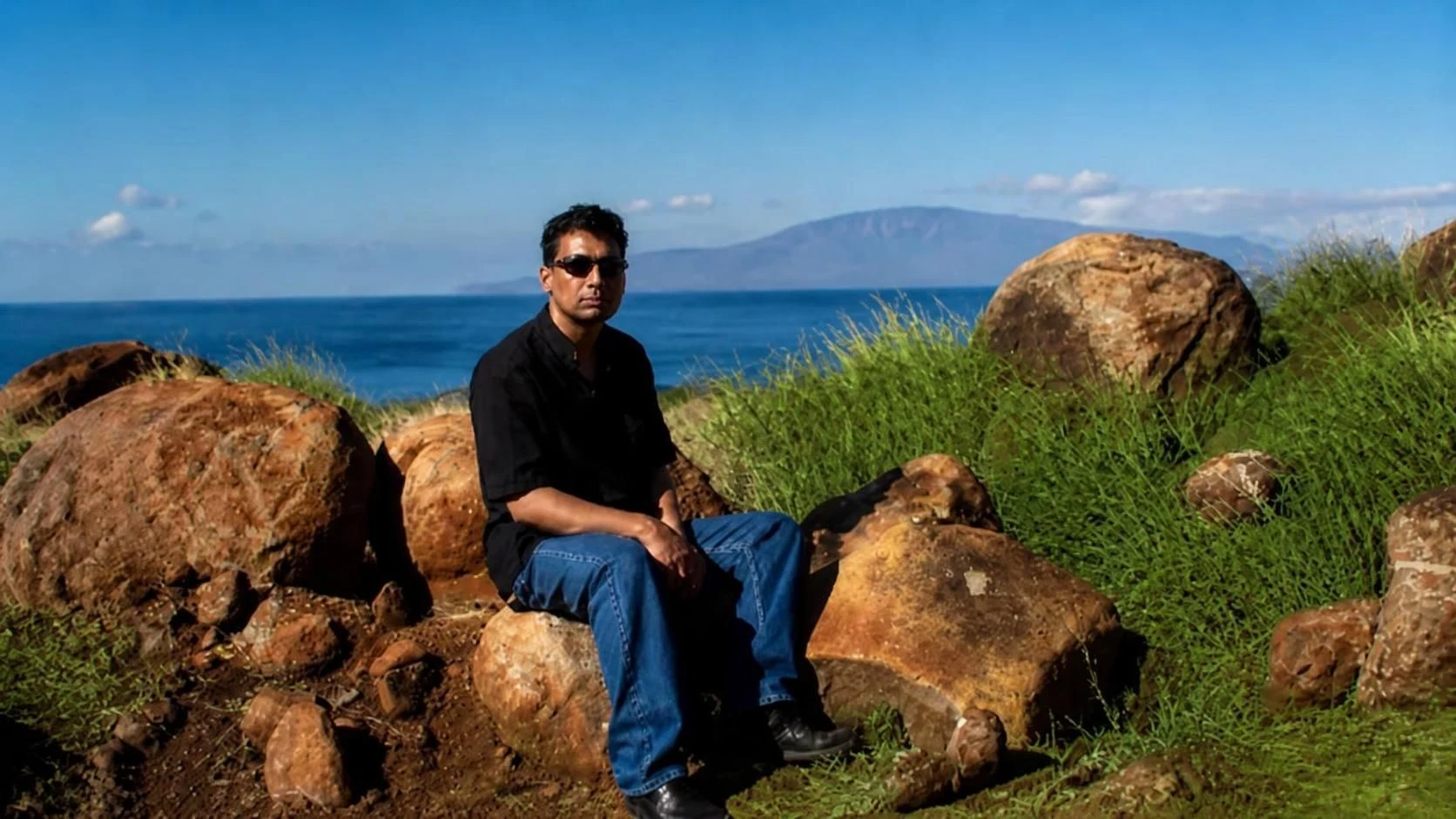 Behleem seated among volcanic boulders above the Hawaii coast